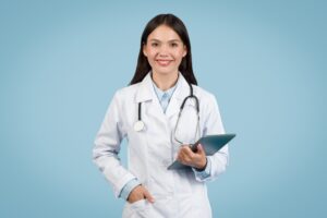 Confident young female doctor with stethoscope around her neck holding digital tablet, ready for patient care, against blue background