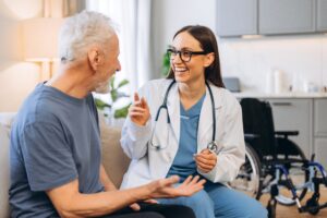 Young female doctor talking happily with an elderly male patient during a home visit, providing personalized medical care